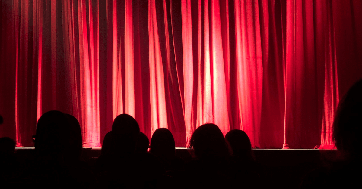 silhouette is people sitting in front of a stage with a red curtain